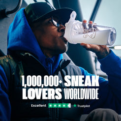 Person drinking from a clear water bottle with a logo, wearing a blue hoodie and cap indoors.